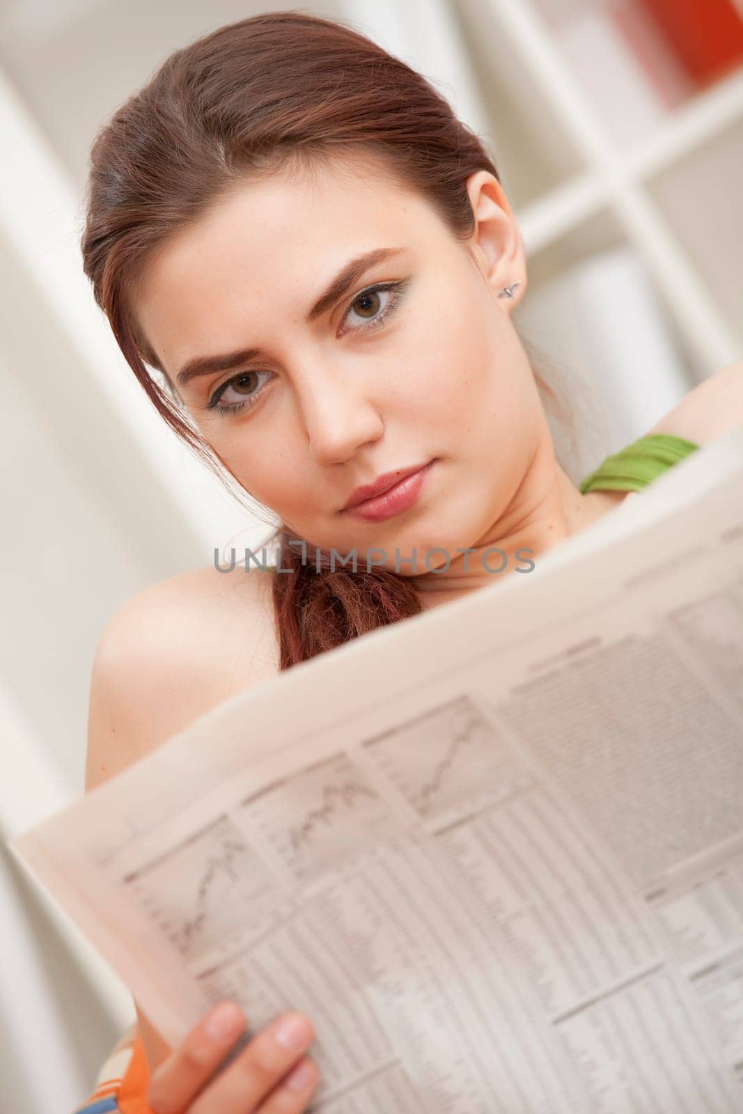 young relaxed woman sitting on sofa with financial newspaper