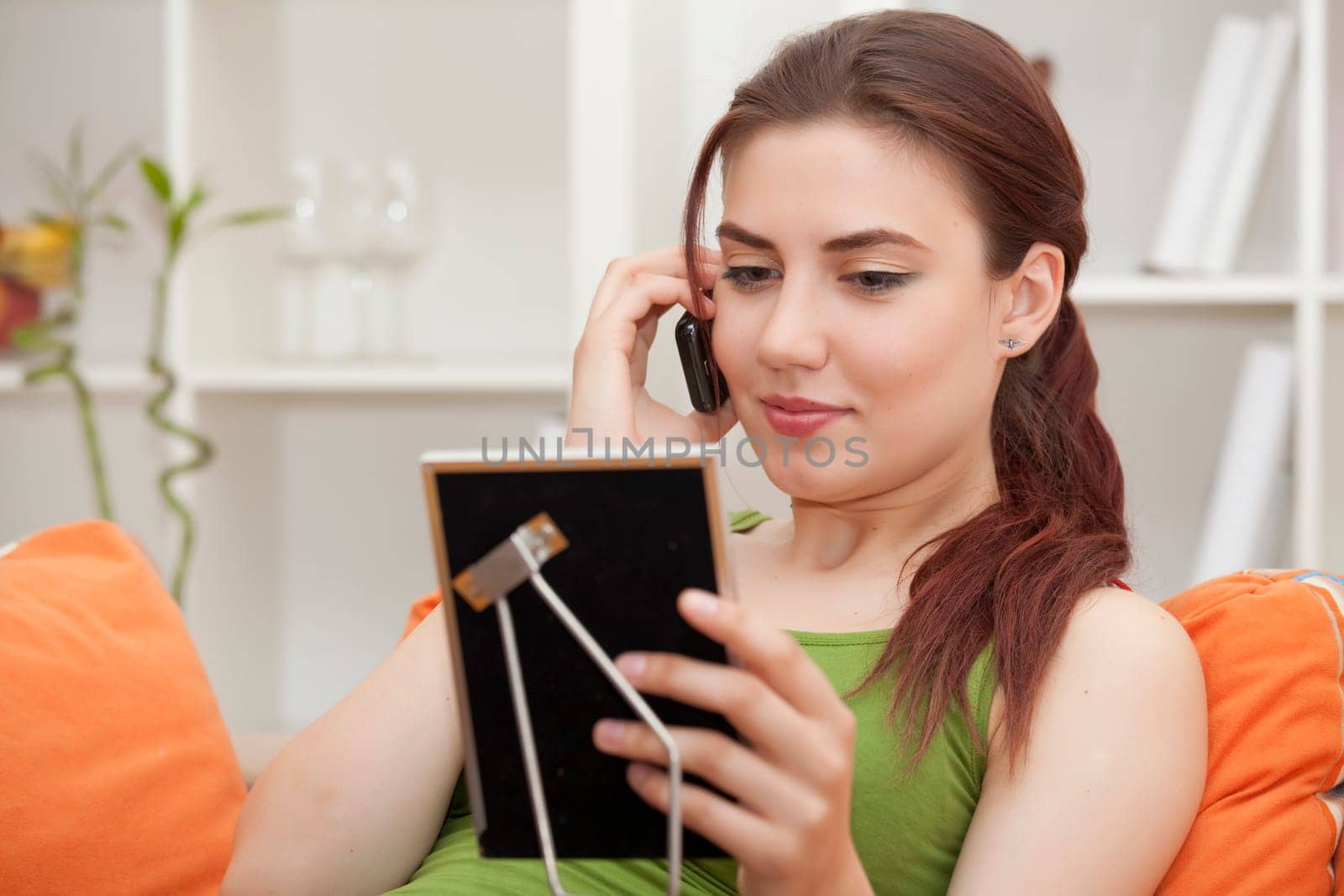 young woman holding phone and picture frame at home