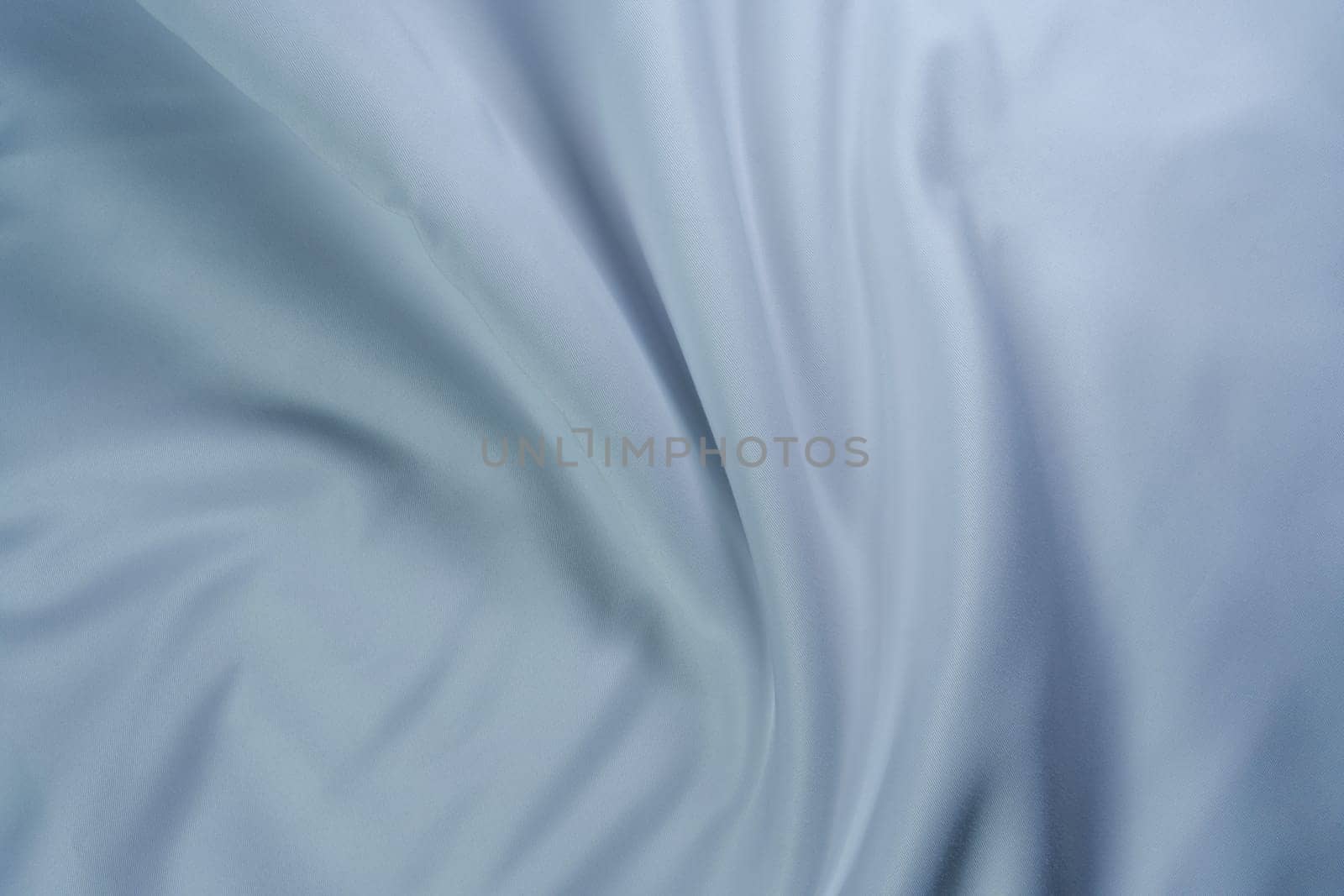 Close-up of soft white fabric with gentle folds creating a swirl pattern, perfect for backgrounds, textures, and design projects.