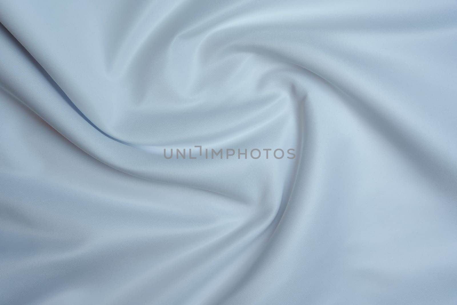 Close-up of soft white fabric with gentle folds creating a swirl pattern, perfect for backgrounds, textures, and design projects.