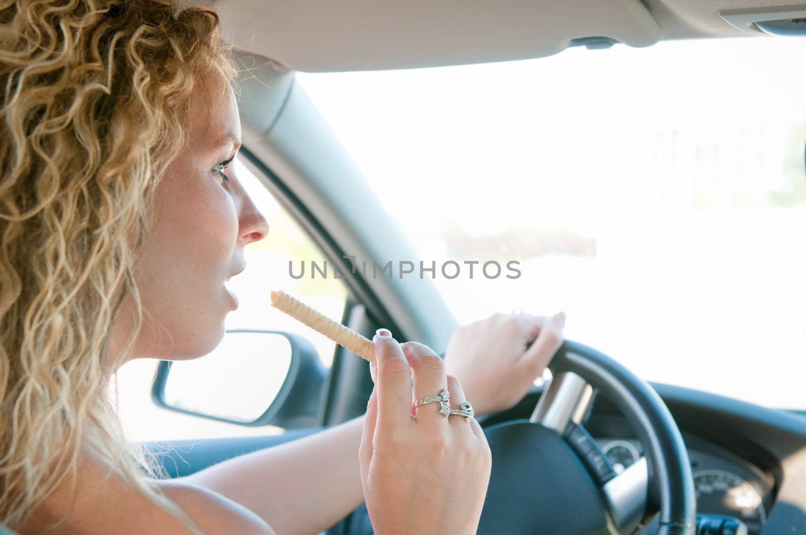 Young woman driving car and eating sweet - rear view