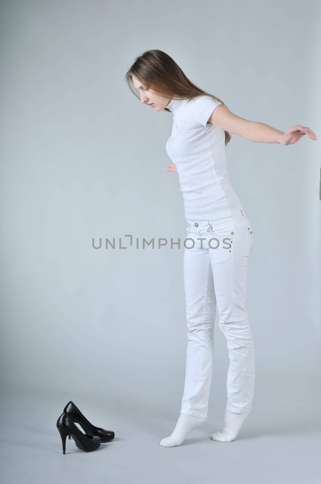 Young woman balancing on toes with high heels shoes placed on floor