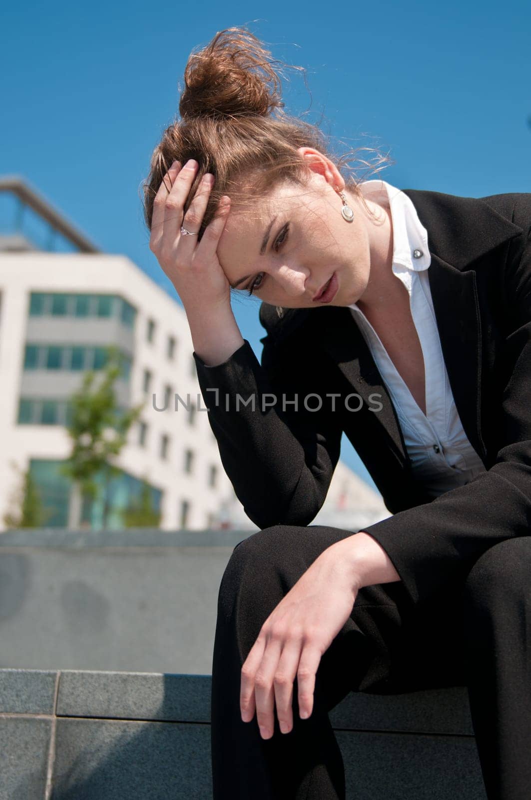 Young worried business woman siting outdoors - head in hand