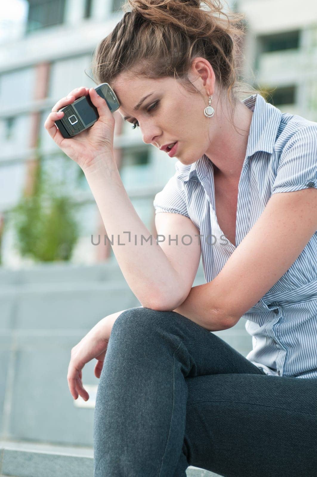 Young worried woman with unhappy expression holding mobile phone - outdoors in urban setting