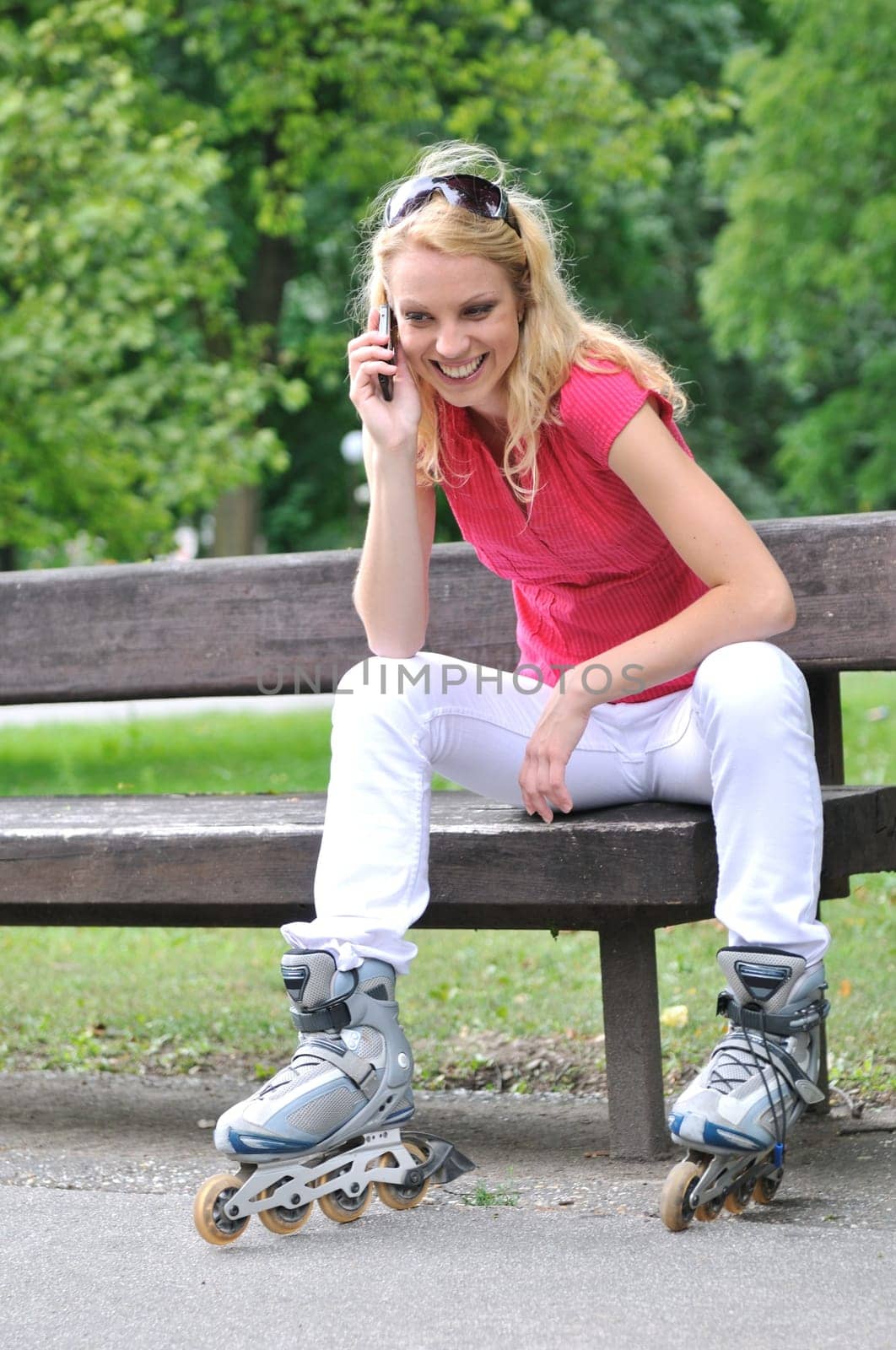 Young smiling woman wearing rollerblades calling with mobilephone outdoors