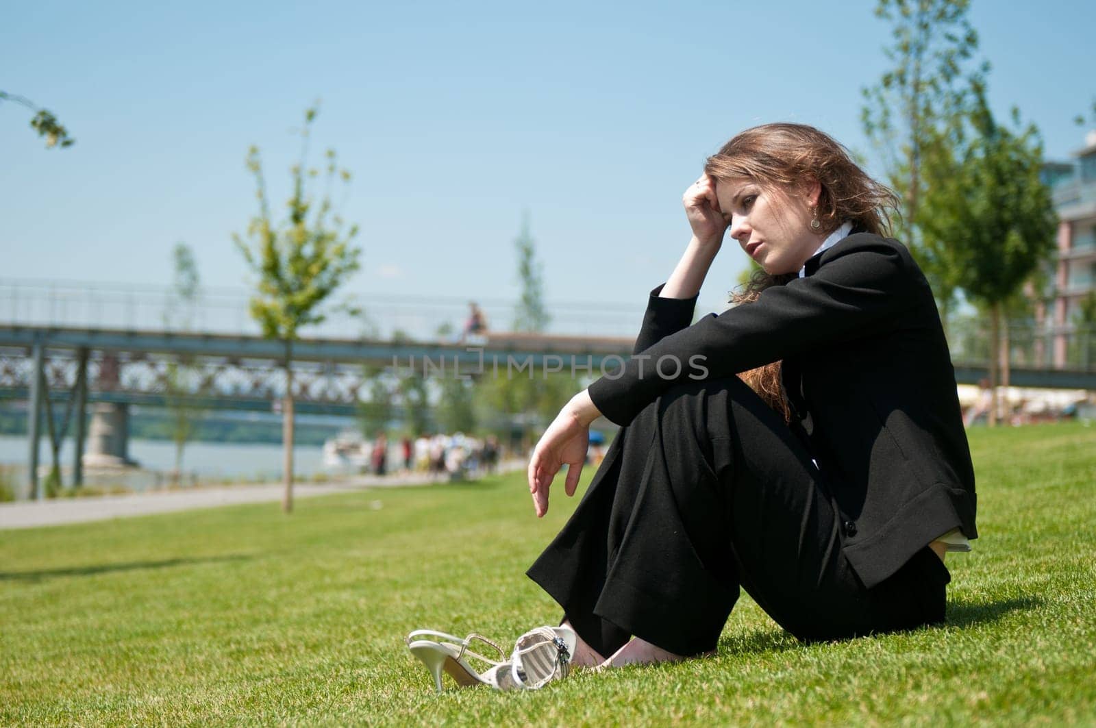 Young worried business woman siting outdoors in grass - head in hand