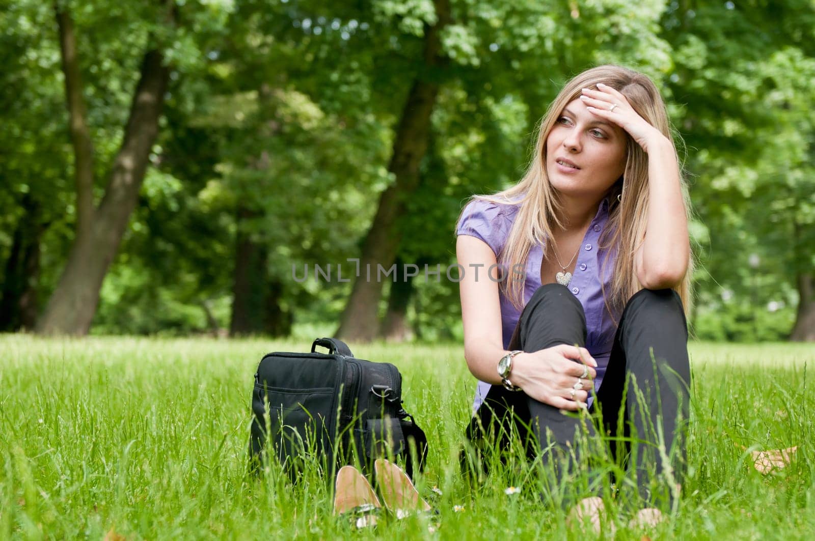 Young worried business woman siting in grass - notebook bag and shoes lying next