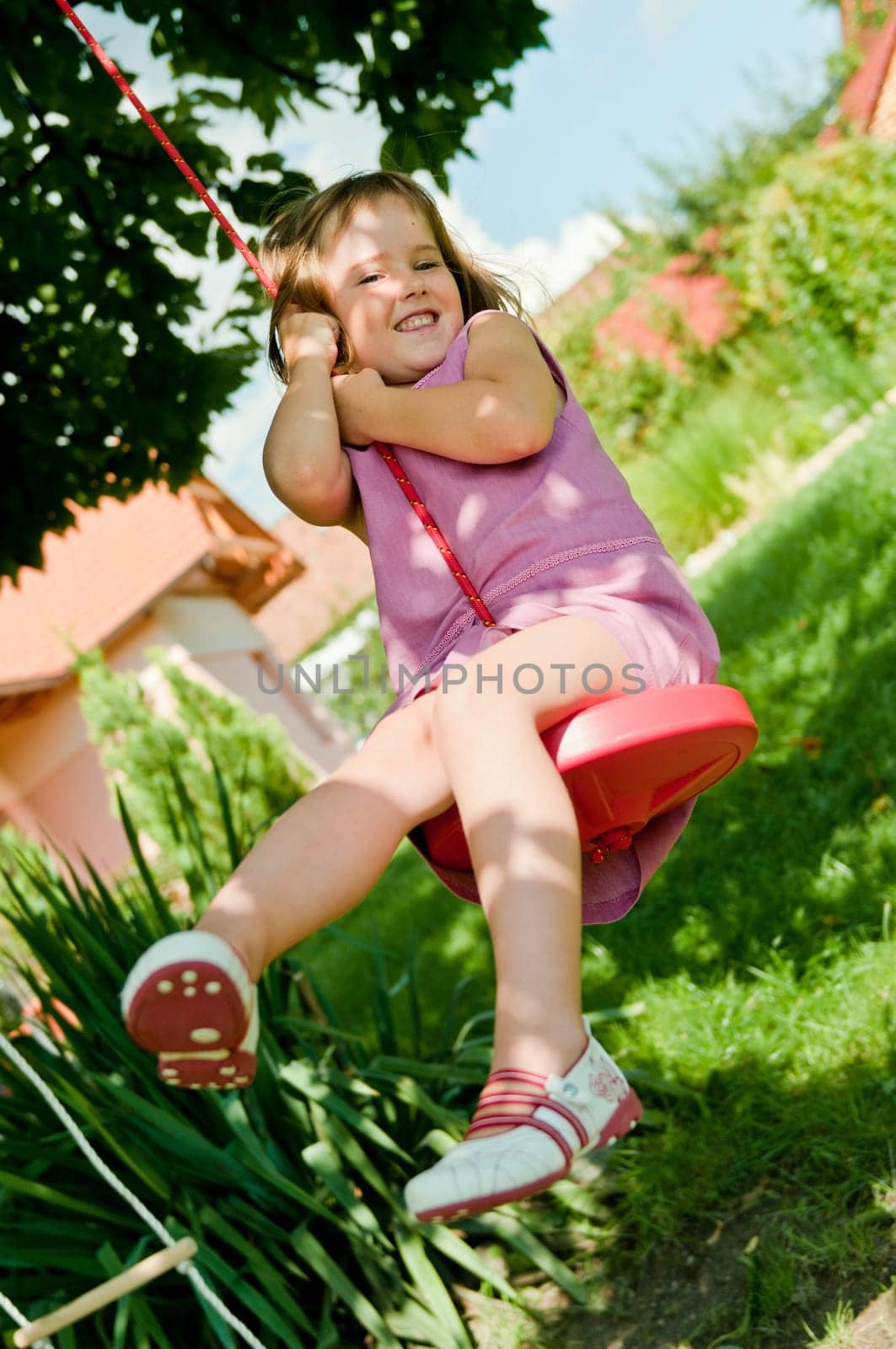 Happy small cute girl swinging on seesaw in garden behind family house