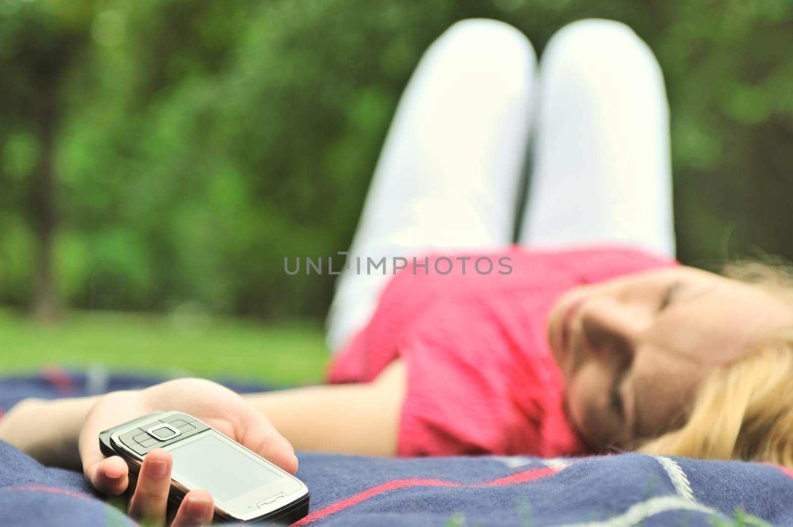 Young woman lying down on rug outdoors with mobile phone in stretched hand
