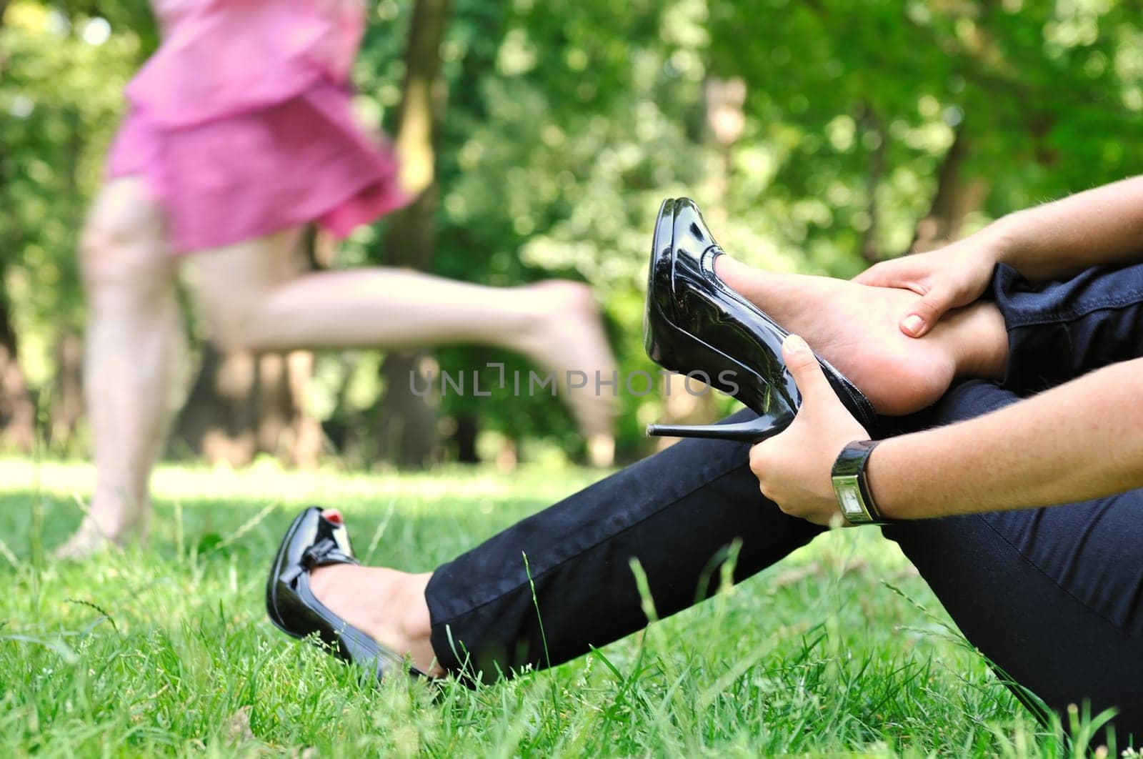 One woman running barefoot in park and second is taking her shoes off