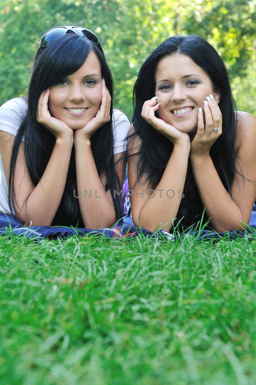 Two smiling friends lying together in grass outdoors with copy space