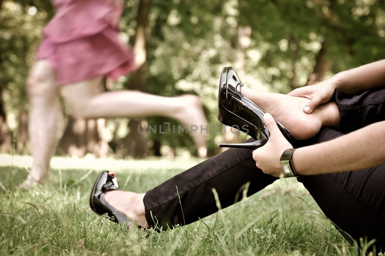 Torso of one woman running barefoot in park and second is taking her shoes off