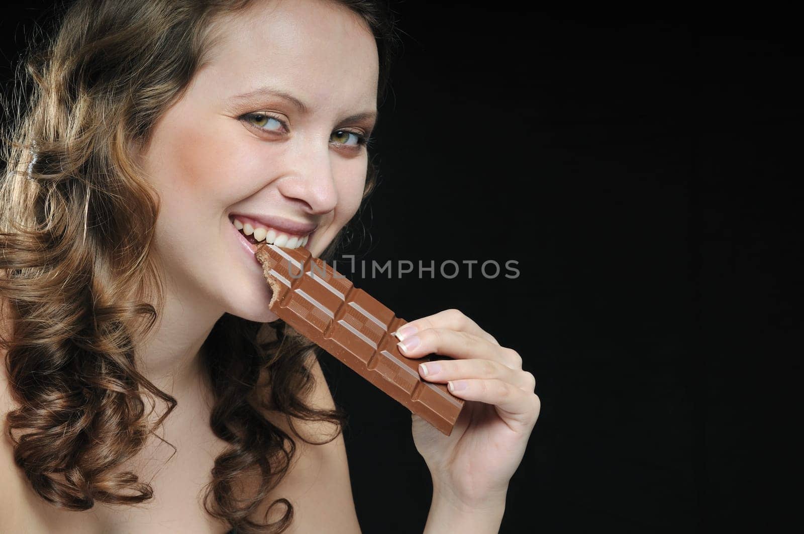 Young beautiful smiling woman eating milk chocolate isolated on black background