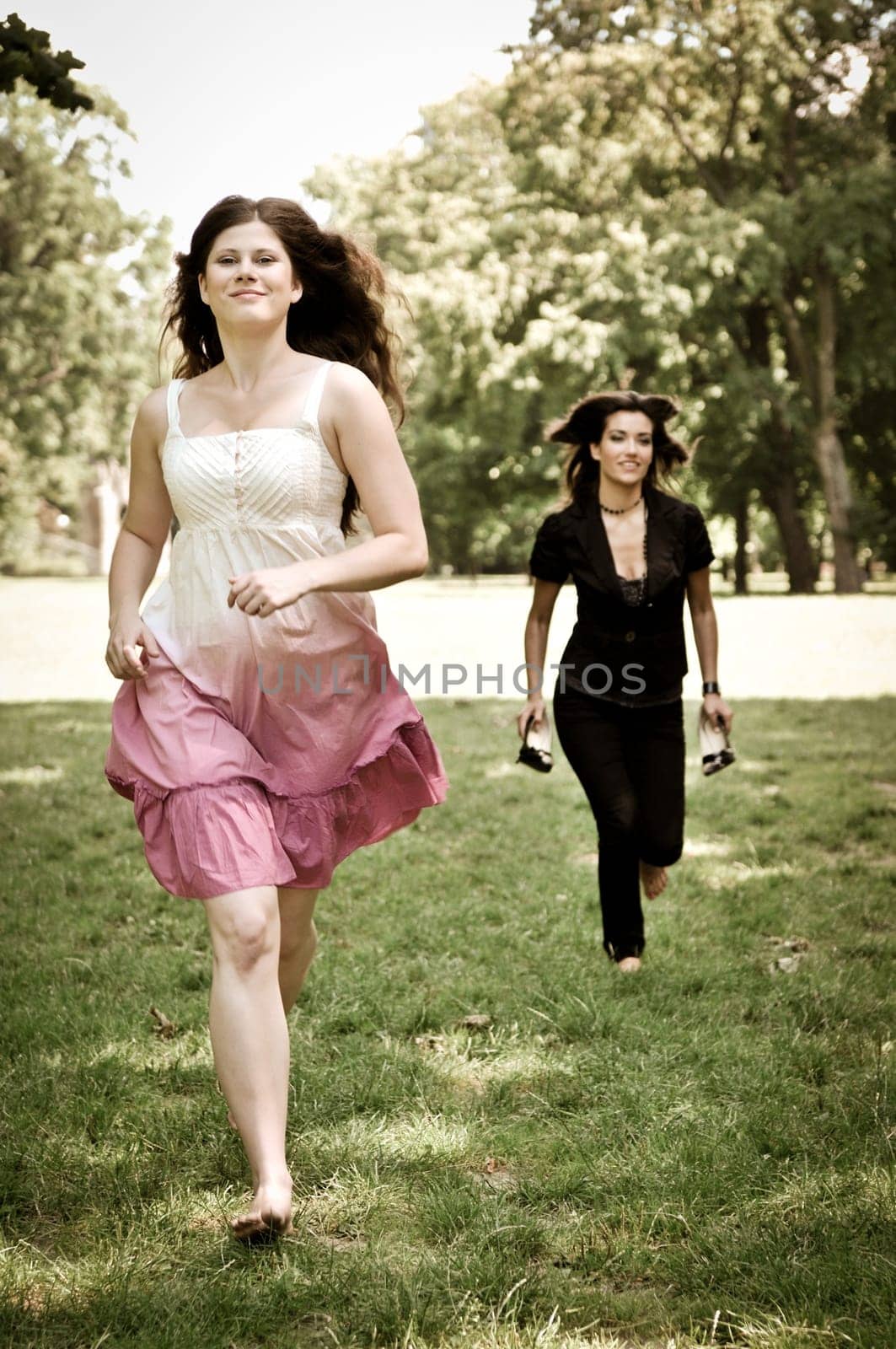 Two friends run barefoot in park on grass - freedom concept