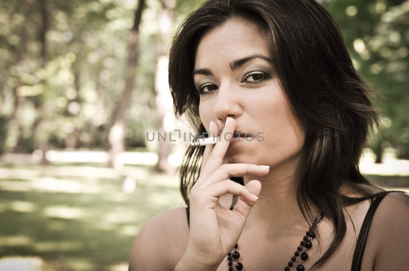 Portrait of young woman smoking cigarette outdoors in sunny green park