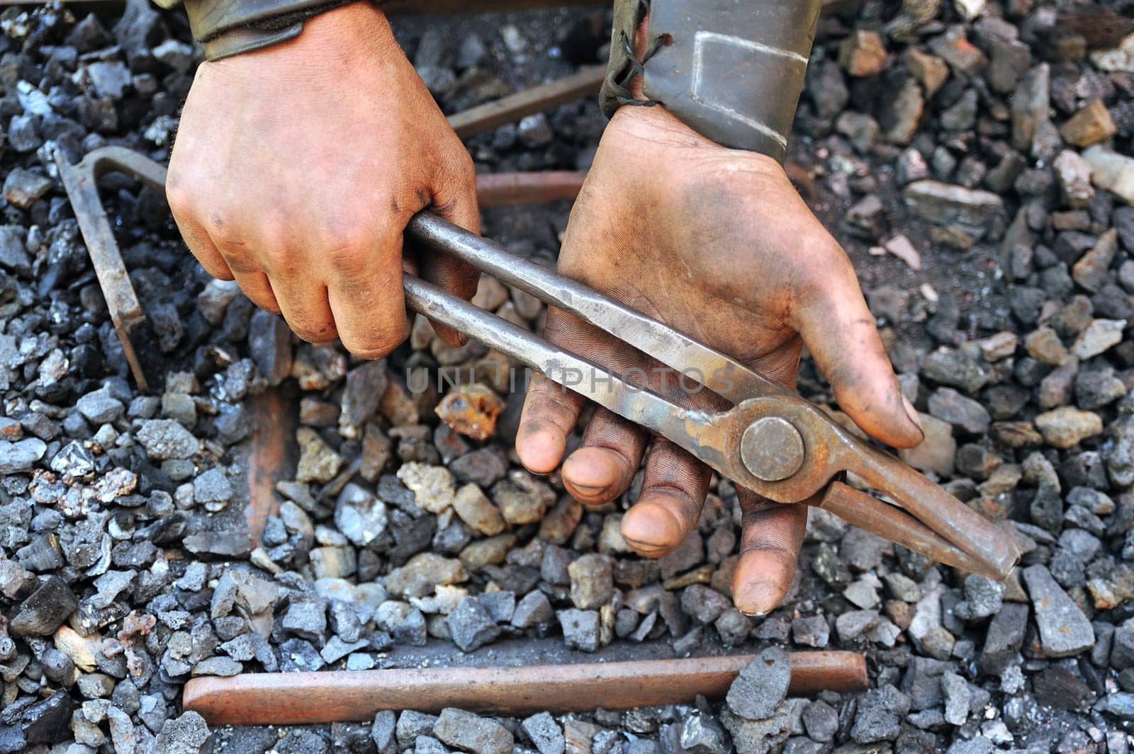 Detail of dirty hands holding pliers - blacksmith