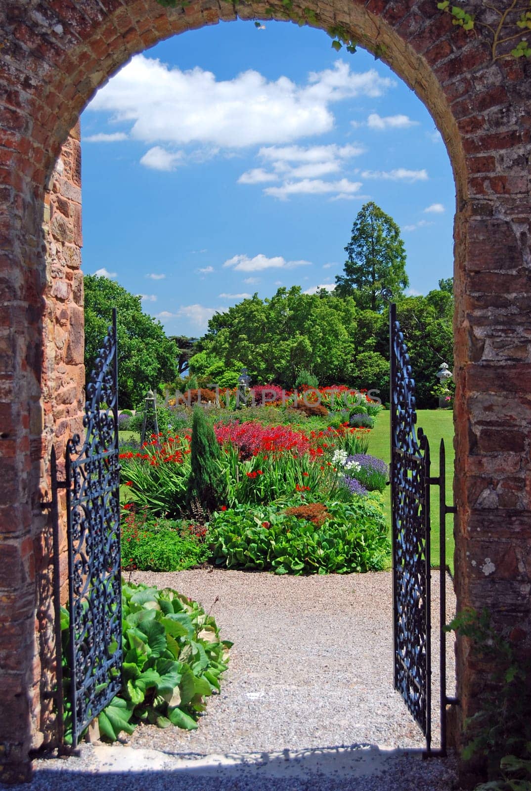 A Summer Garden through an archway in a Stately Home in Devon showing formal flower gardens and a blue sky