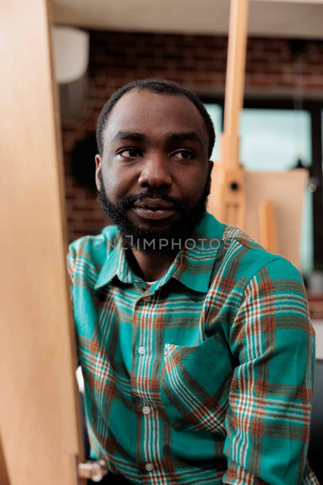 Creativity and self expression through art. Portrait of African American guy sitting at easel exploring creativity with drawing lessons, smiling young black man visiting painting class for adults