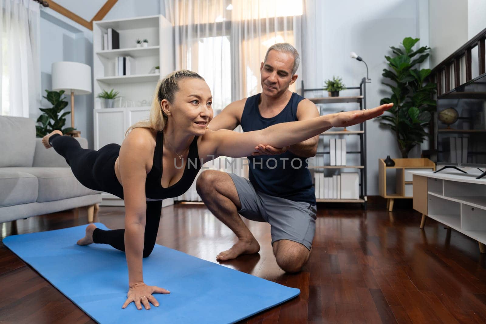 Happy active senior couple in sportswear being supportive and assist on yoga posture together at home. Healthy senior man and woman lifestyle with yoga exercise. Clout