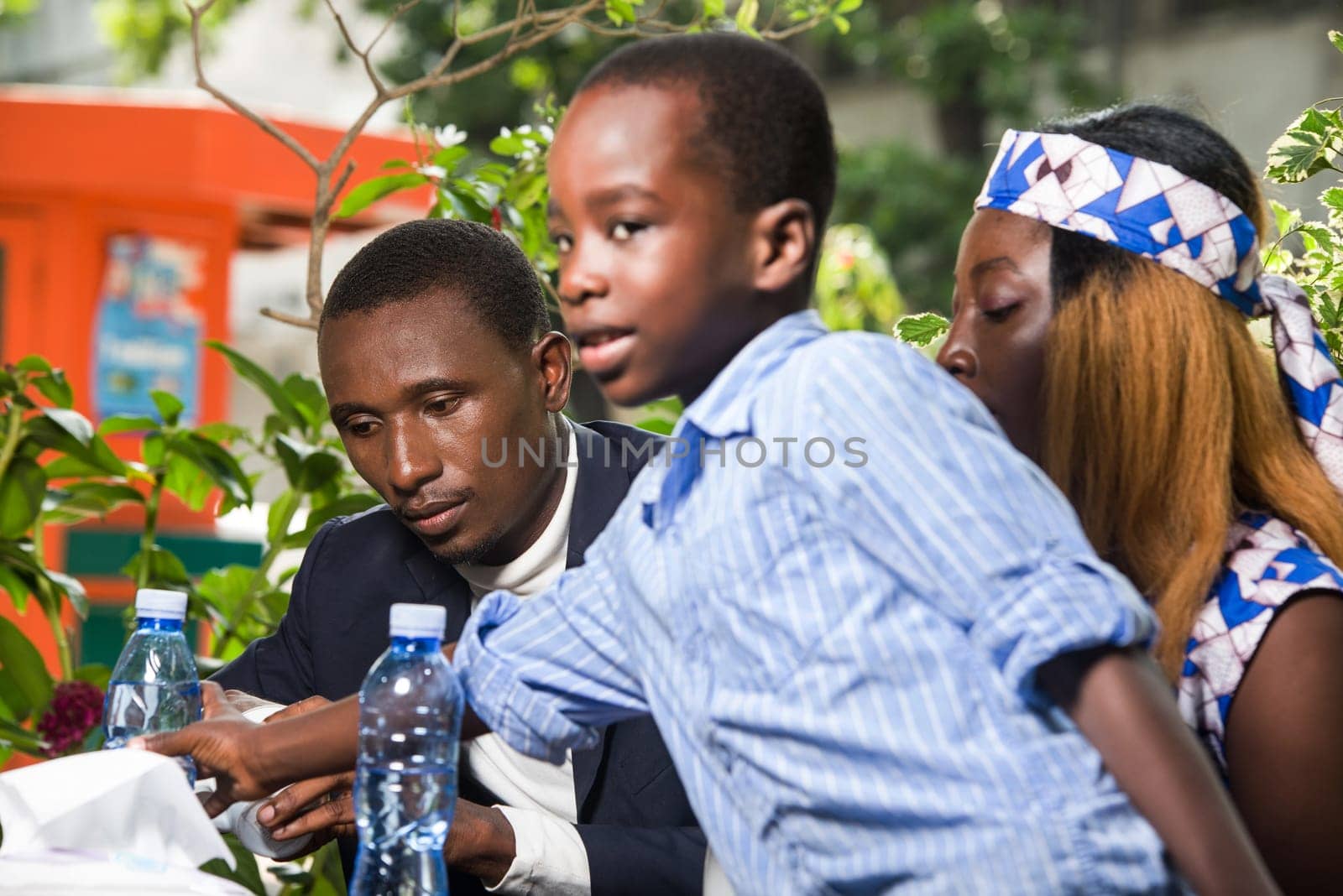 a couple sitting in a park watching their son take a bottle of water.