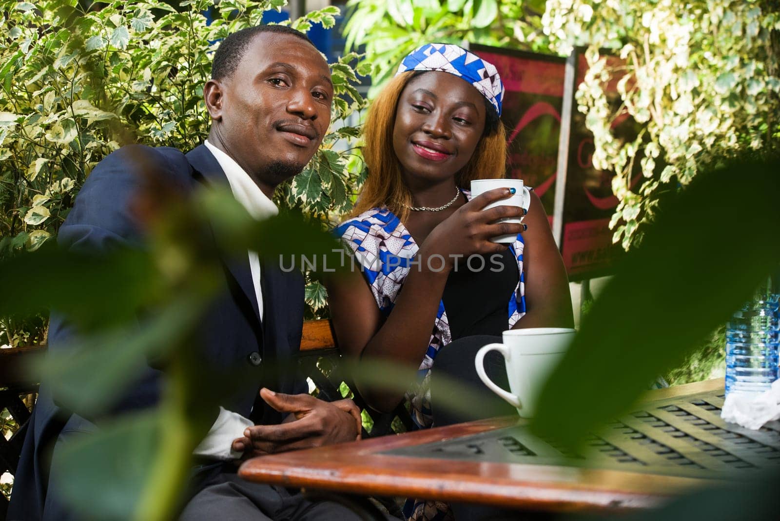 young couple sitting in a park drinking tea while smiling.