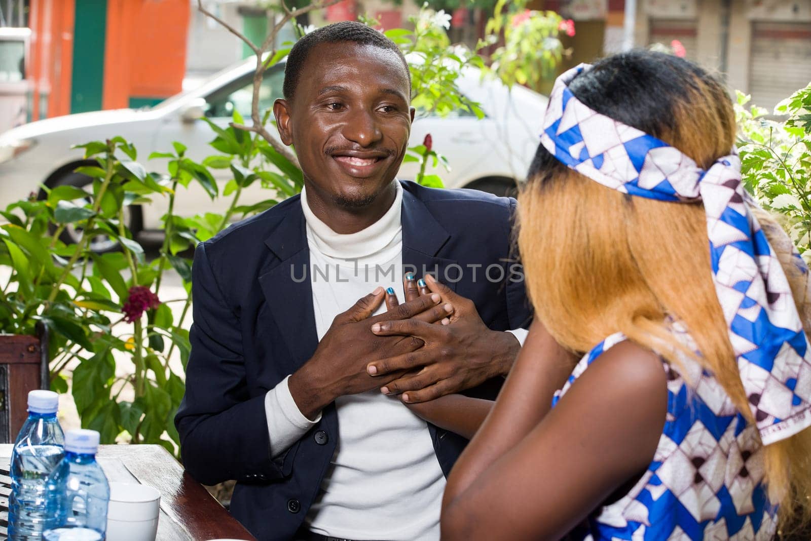 Happy couple sitting on a cafe terrace flirting while having a conversation and looking at each other in a restaurant. man in a suit holds his girlfriend's hand and declares his love