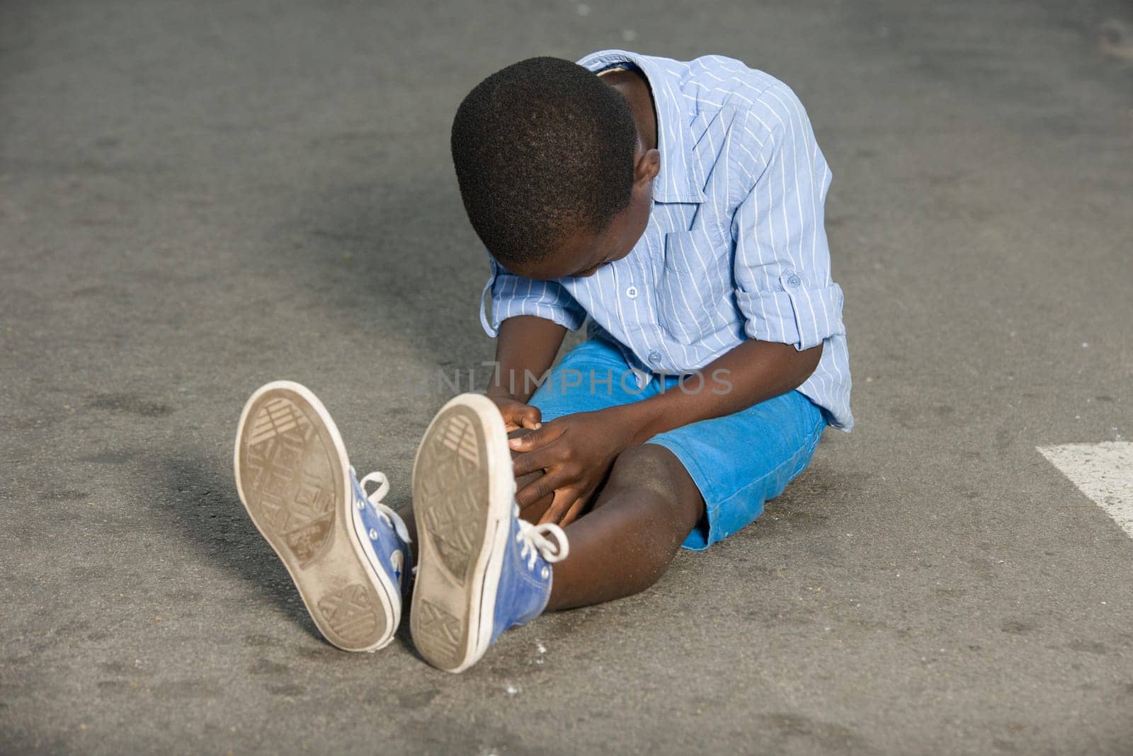 Little boy falling and crying on the road. child sitting alone in the middle of the road with knee ache and waiting for help looking at his injury