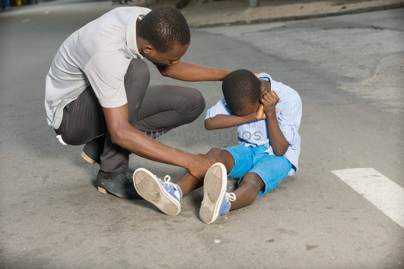 Father comforting his son crying, child fallen on the road having a knee injury