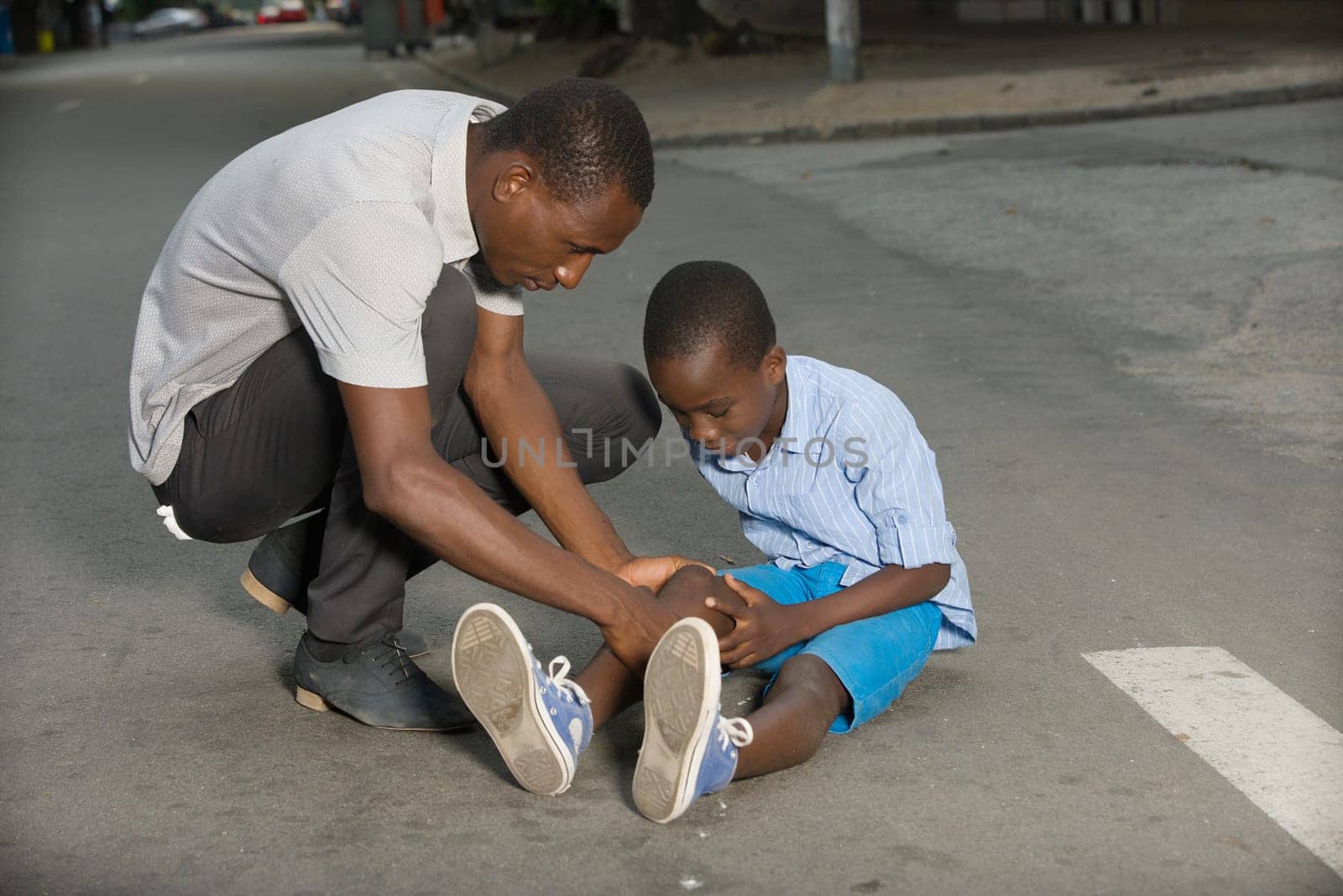 Father comforting his son crying, child fallen on the road having a knee injury