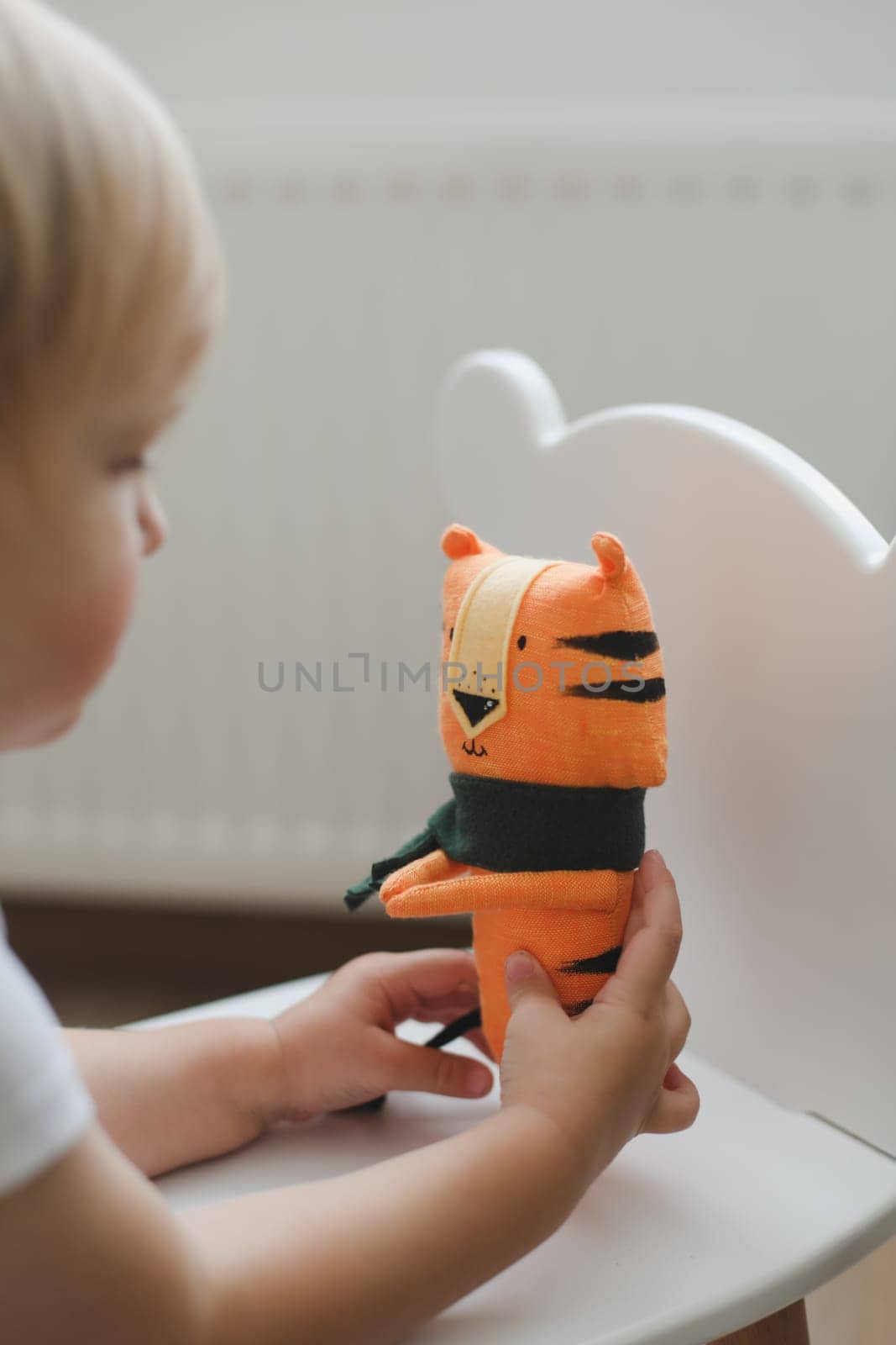 Little baby playing with funny small tiger toy, symbol of new 2022 in a sunny nursery