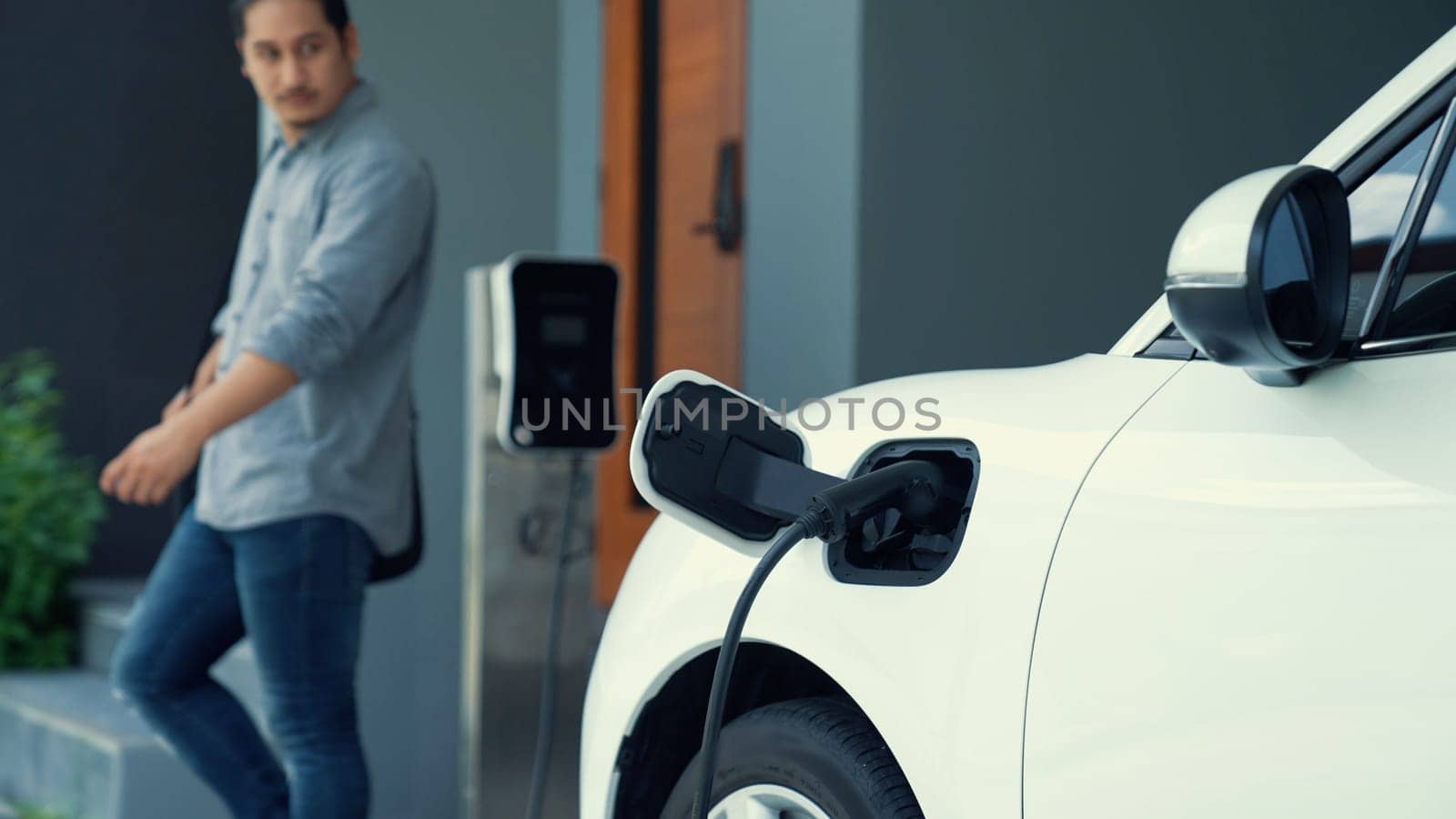 Progressive man unplugs the electric vehicle's charger at his residence. by biancoblue