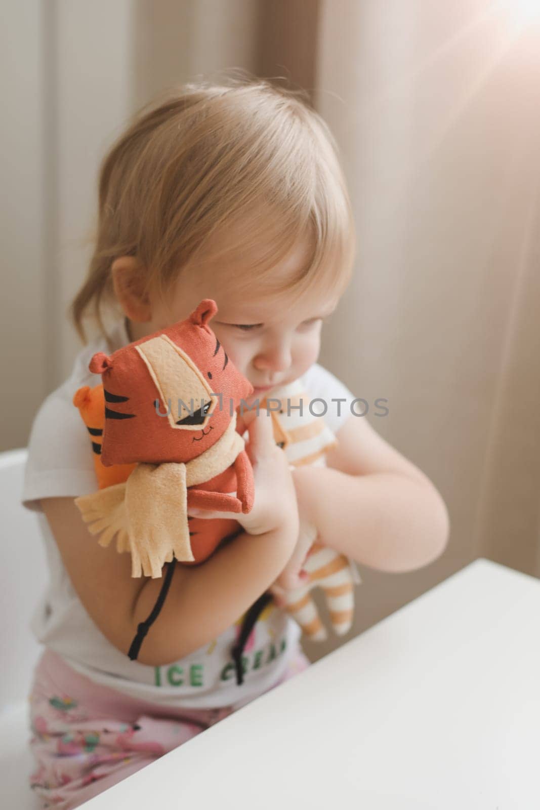 Little baby girl playing with funny small tiger toy, symbol of new 2022 in a sunny nursery by paralisart