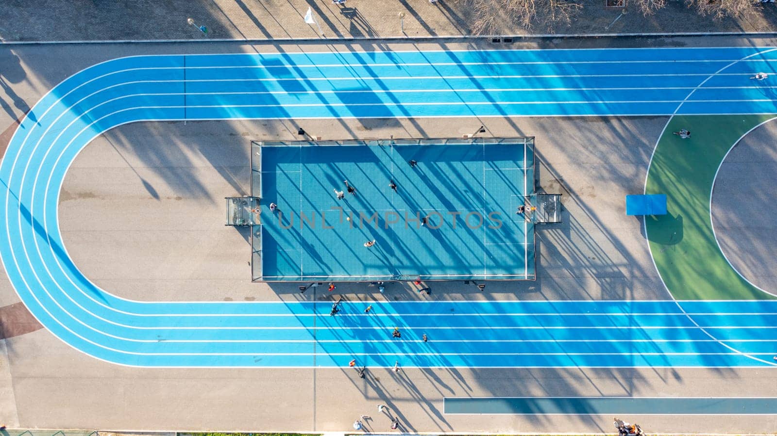 Aerial drone top view of running track mini football soccer field with artificial plastic cover with playing people. Public sport ground in city at sunny summer day drone view