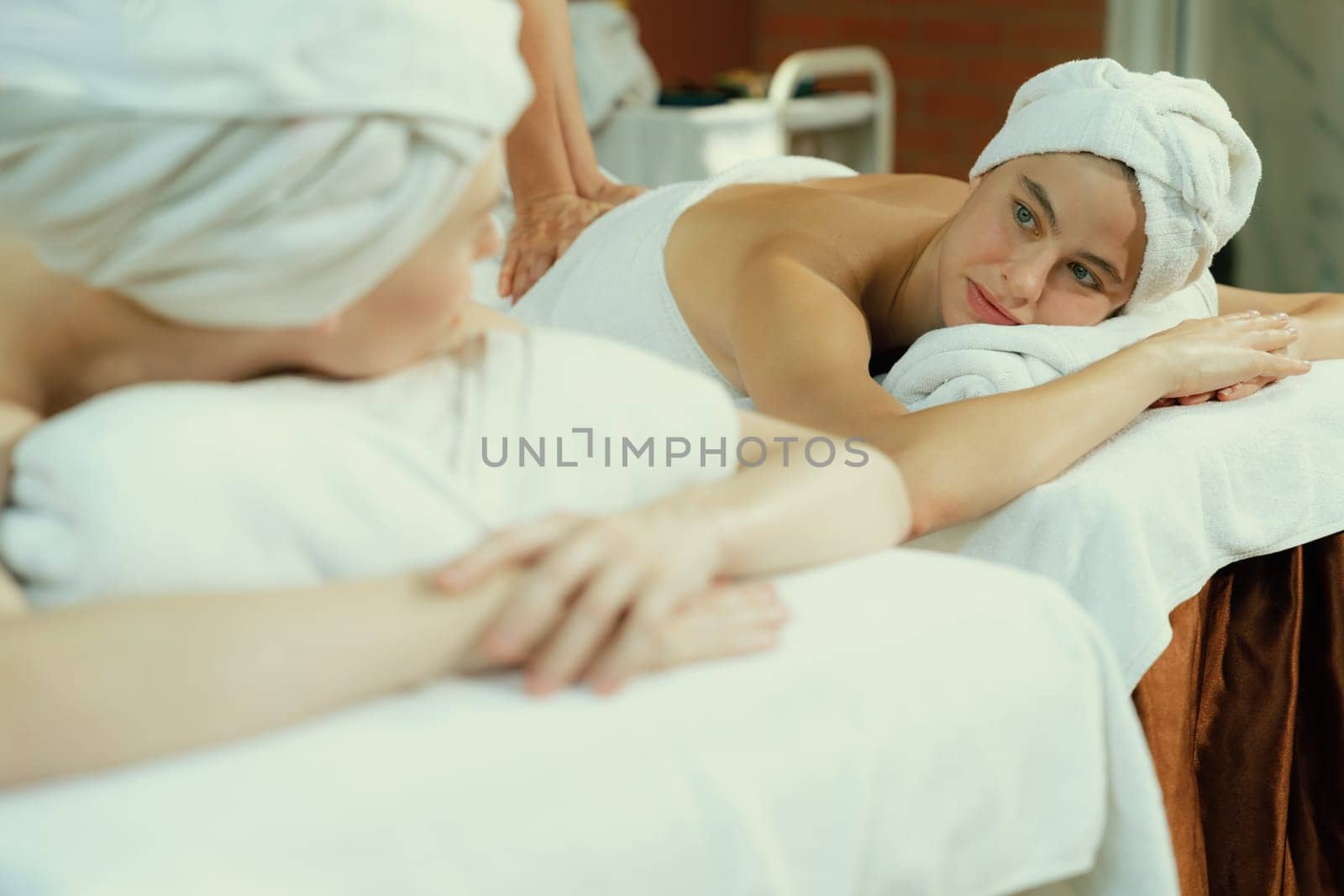 A portrait of two attractive young women with beautiful skin in white towel having a back massage by professional masseur at traditional spa salon. Beauty and healthy. Tranquility.