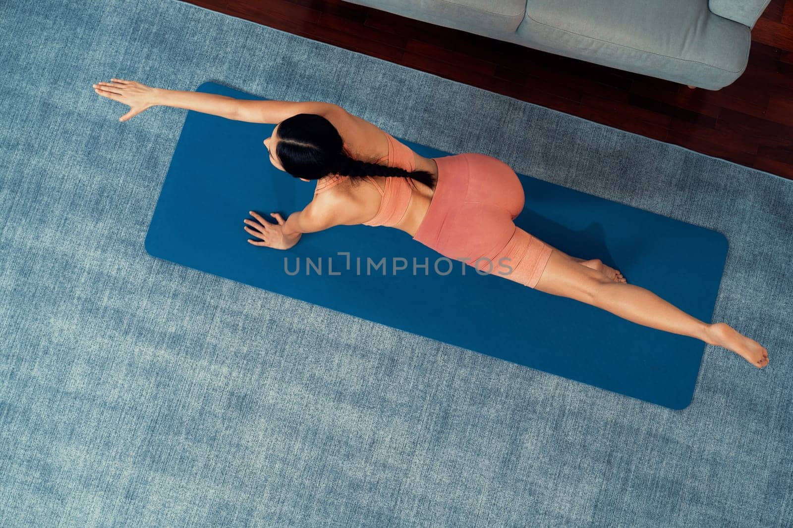 Top view asian woman in sportswear doing yoga exercise on fitness mat as her home workout training routine. Healthy body care and calm meditation in yoga lifestyle. Vigorous