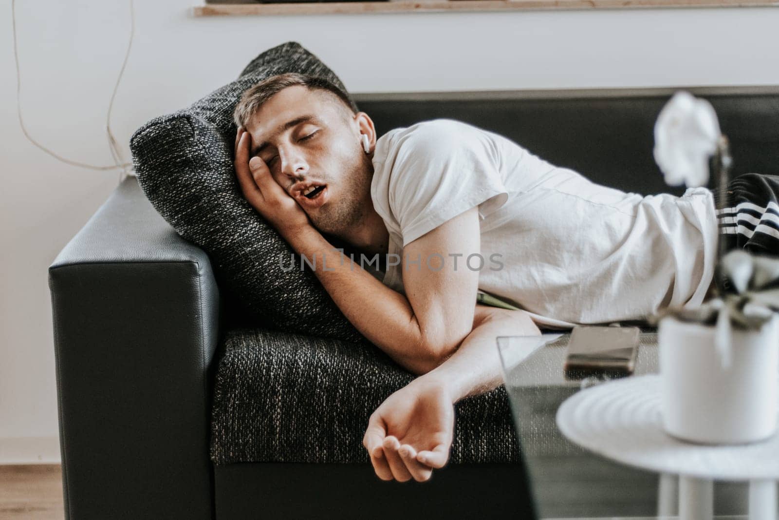 One young Caucasian handsome guy sleeps soundly with his mouth open while lying on the sofa in the salon on a summer day, close-up side view in slow motion.
