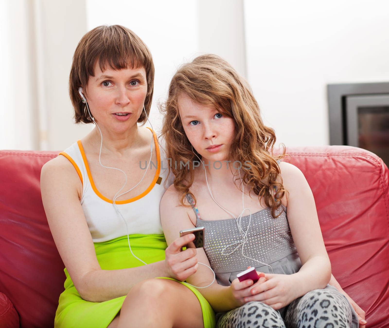 Mother and teenager daughter sitting on sofa together and listening mp3 players
