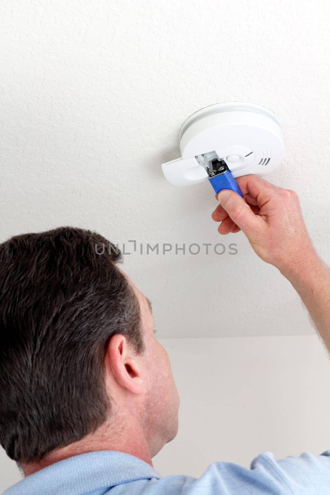 Man carefully replacing 9 volt battery in round white ceiling smoke alarm detector for the safety of his household.