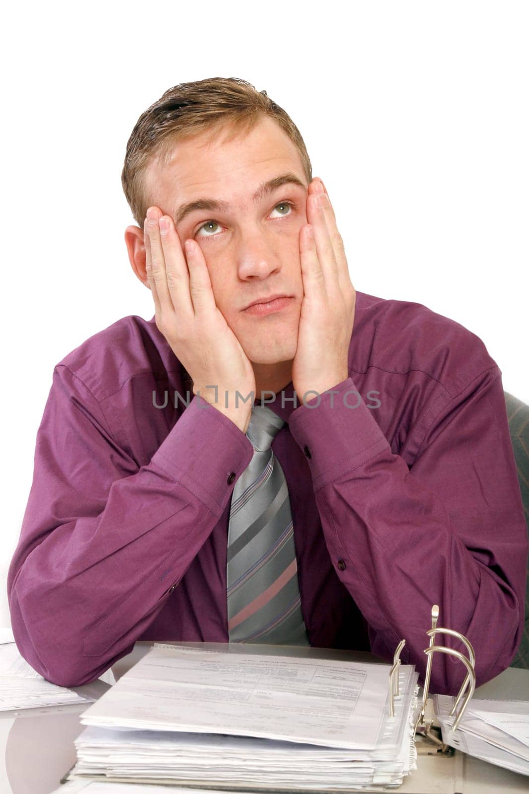 Exhausted man in office with files in front of him. He holds his hands to his face and looks up sadly