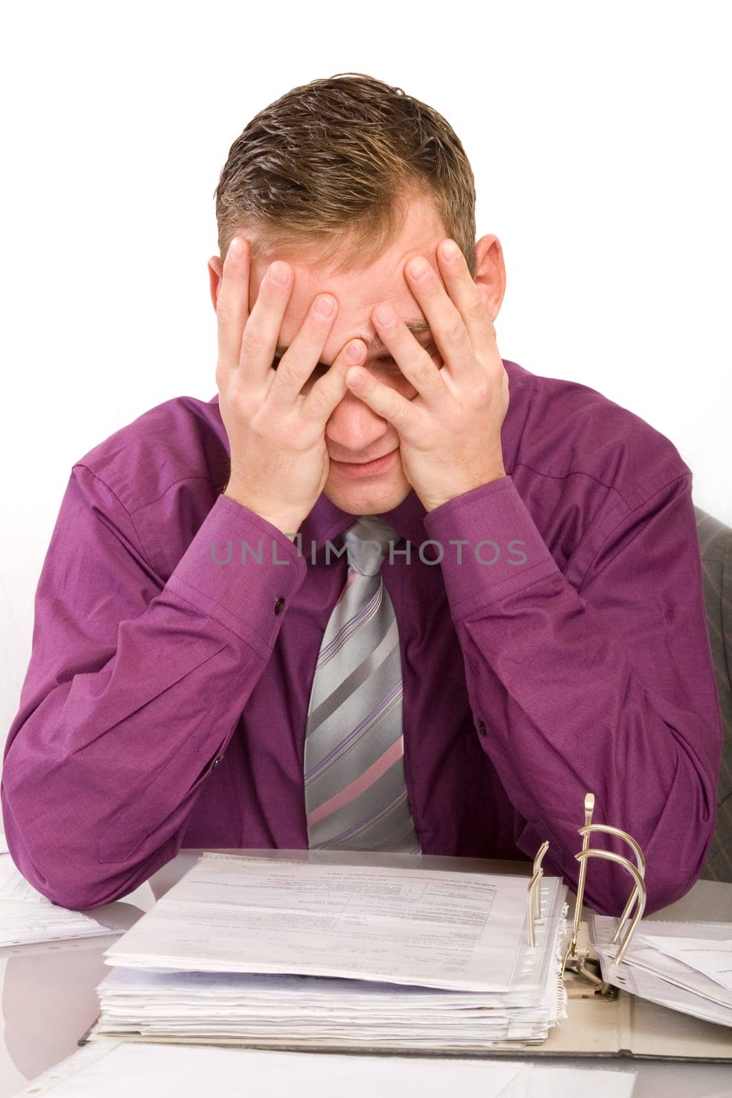 Overwhelmed and desperate businessman in the office. He sits in front of a file folder and holds his hands in front of his face.