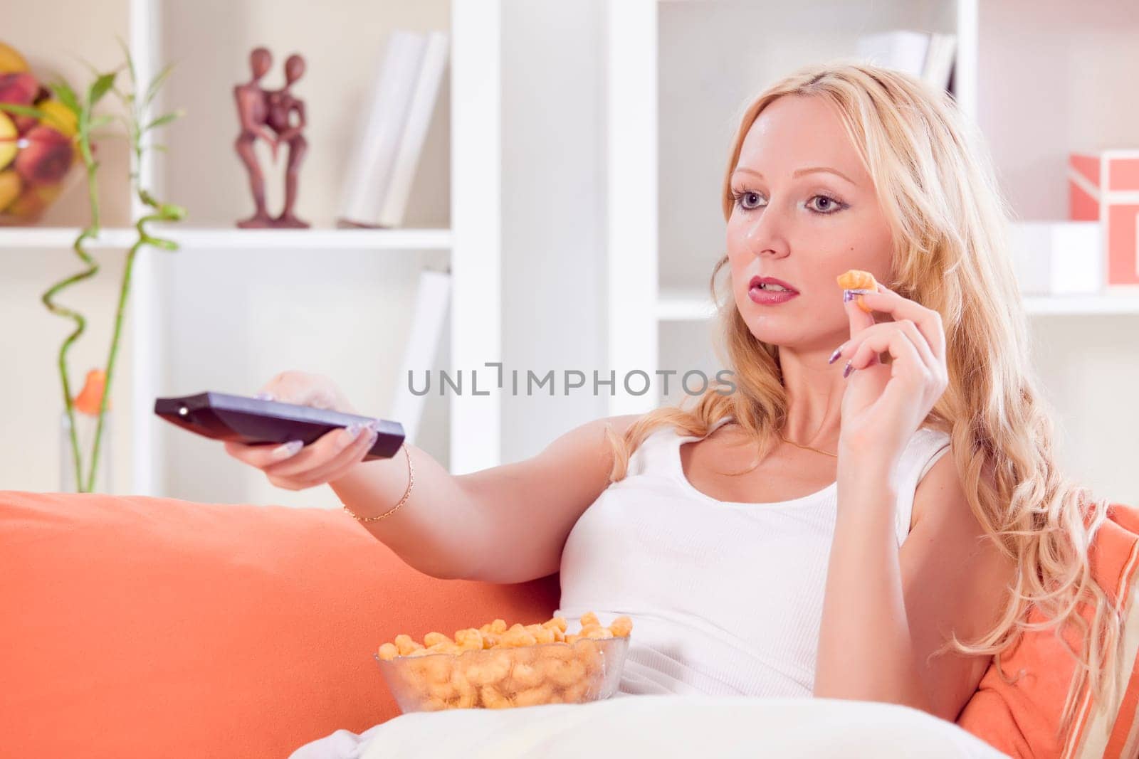 woman with remote control and chips watching television on sofa