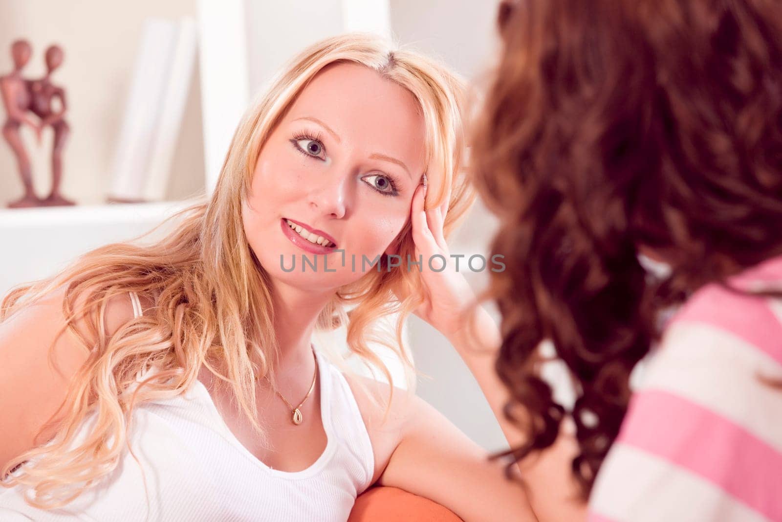 two women friends talking while sitting on sofa at home