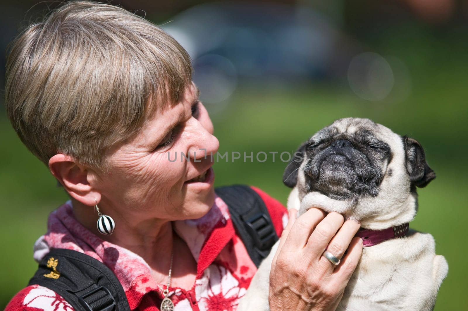 Head and shoulders view of a mature woman with dog (pug) in her arms and looking at the dog and scratching the dog's neck
