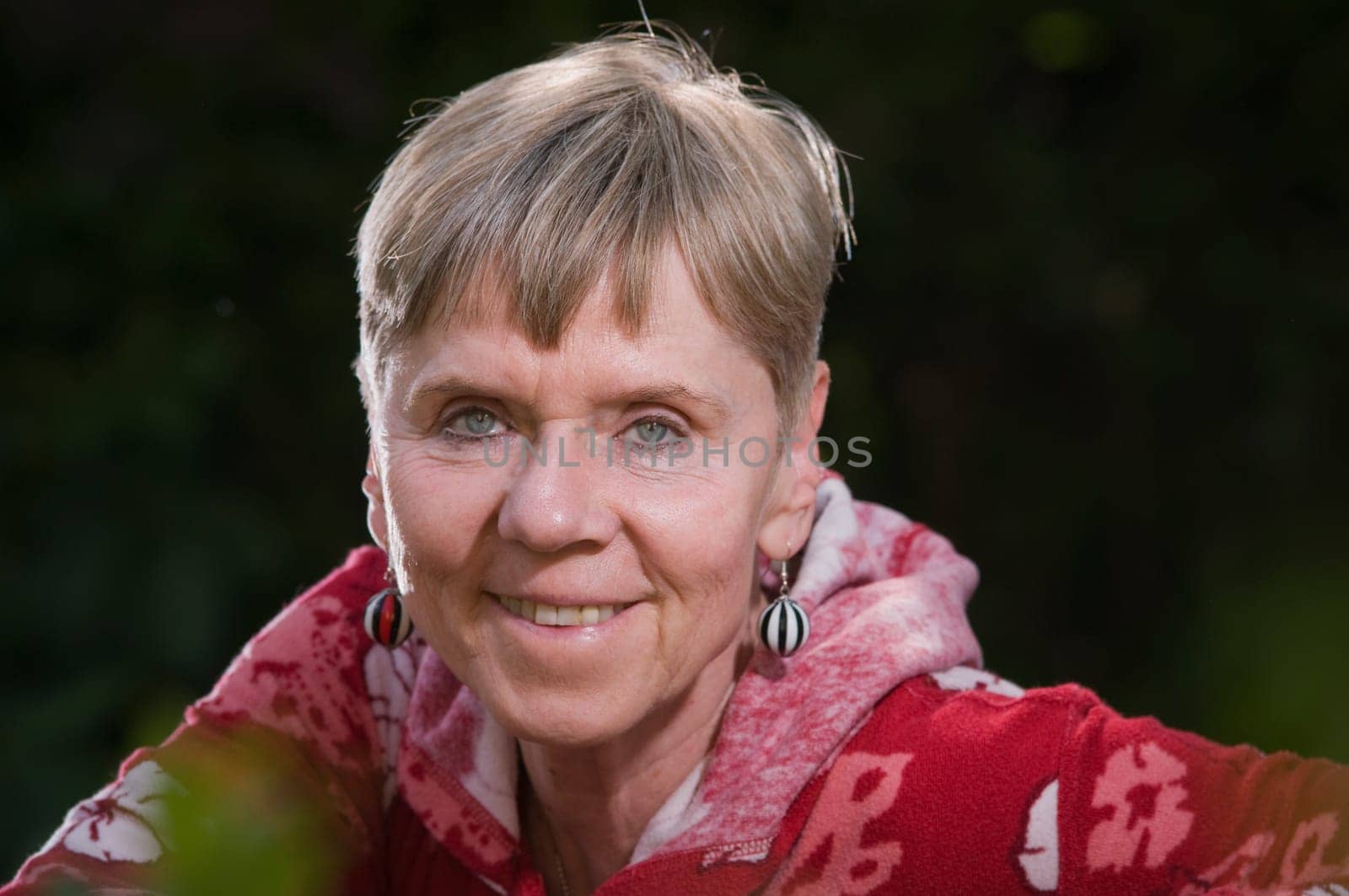 Portrait of an elderly woman on a park bench in summer with her torso turned backwards over the backrest looking towards the camera