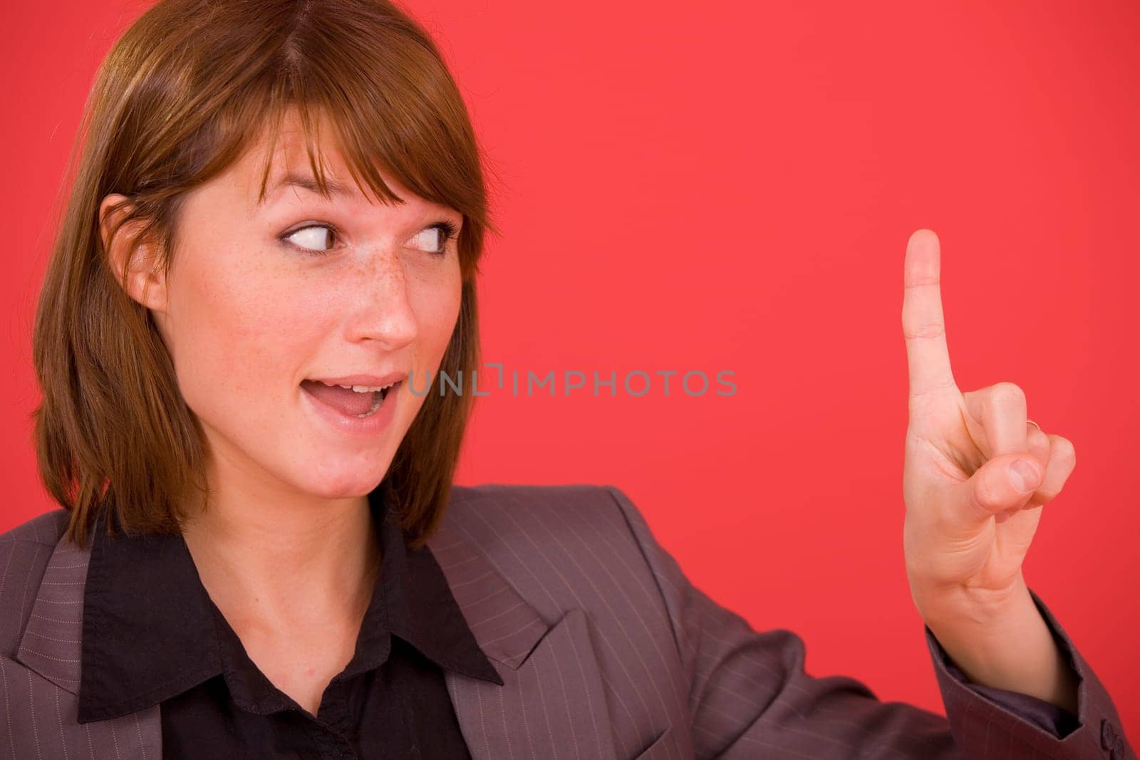 smiling woman gesturing as if she has an idea with raised finger, on red background