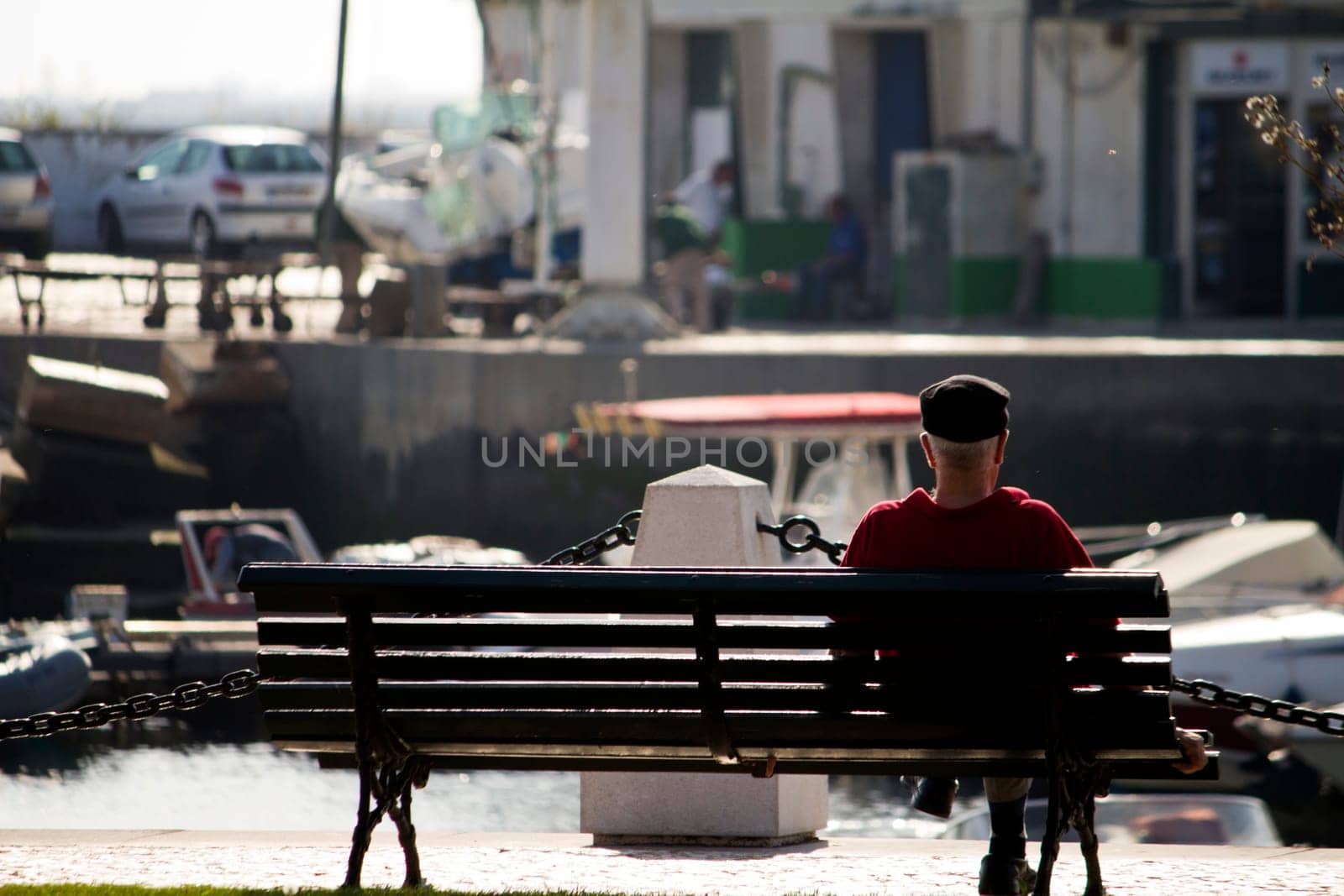 View of a old man relaxing on a bench next to a marina.