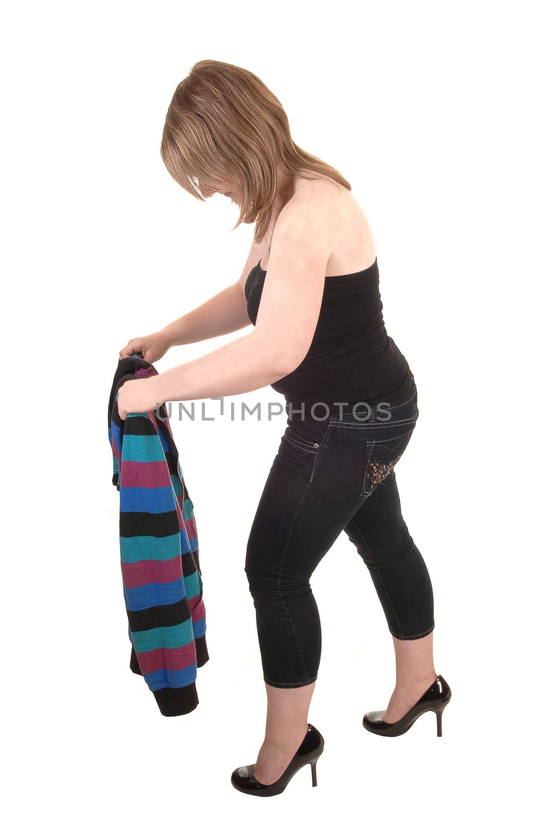 A teenager, in profile, folding her jacket, in jeans and high heels for white background.
