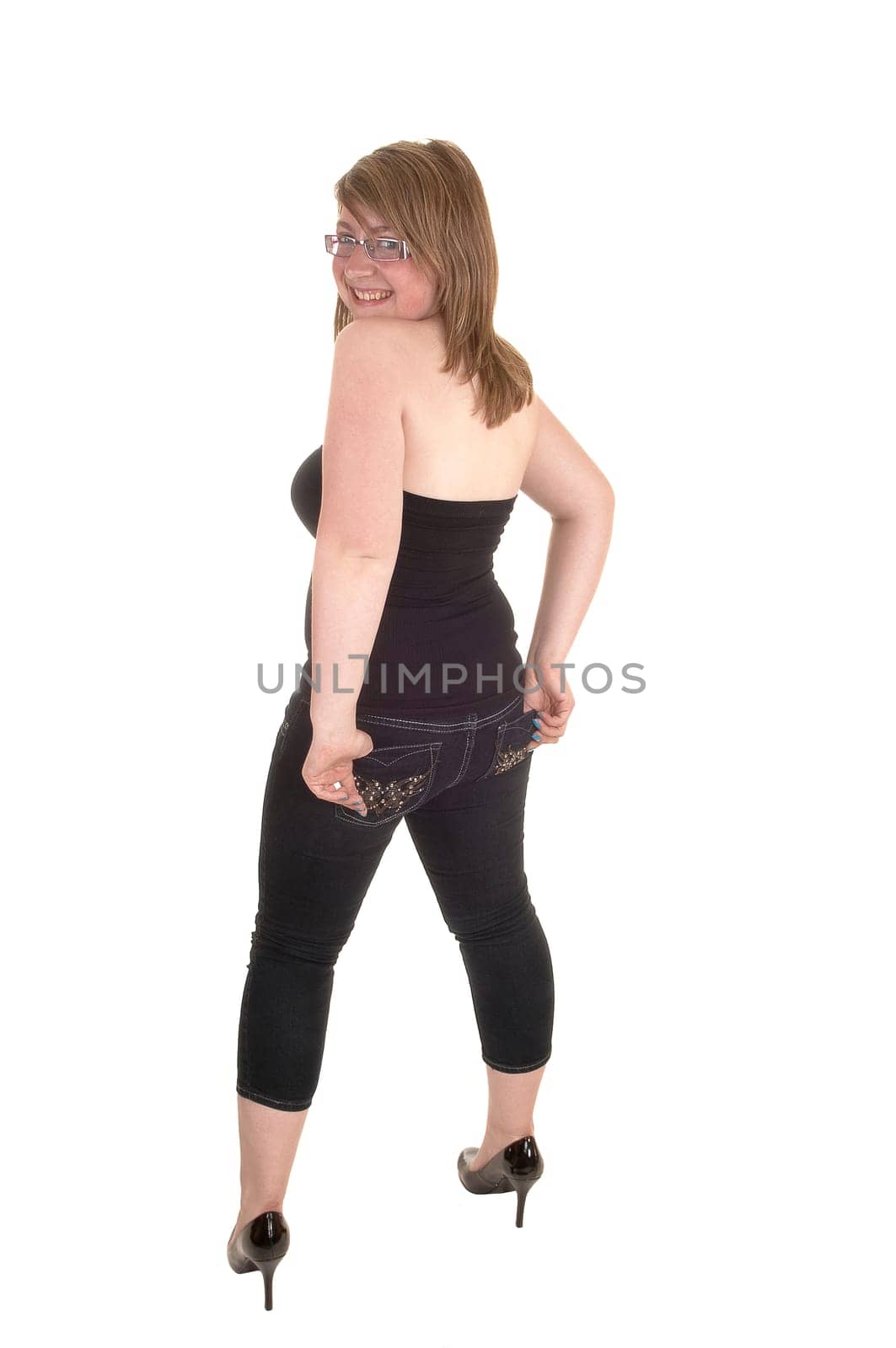 From the back, a teenager standing in the studio in jeans and high heels, looking over her shoulder, for white background.