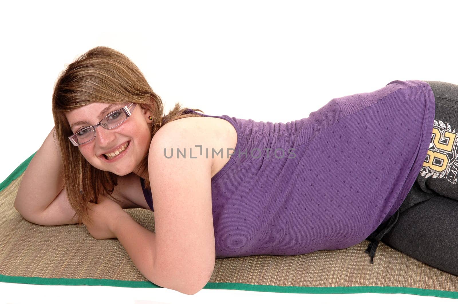Teenage girl lying on a yoga matt on the floor, resting and having a good time, smiling into the camera, for white background.