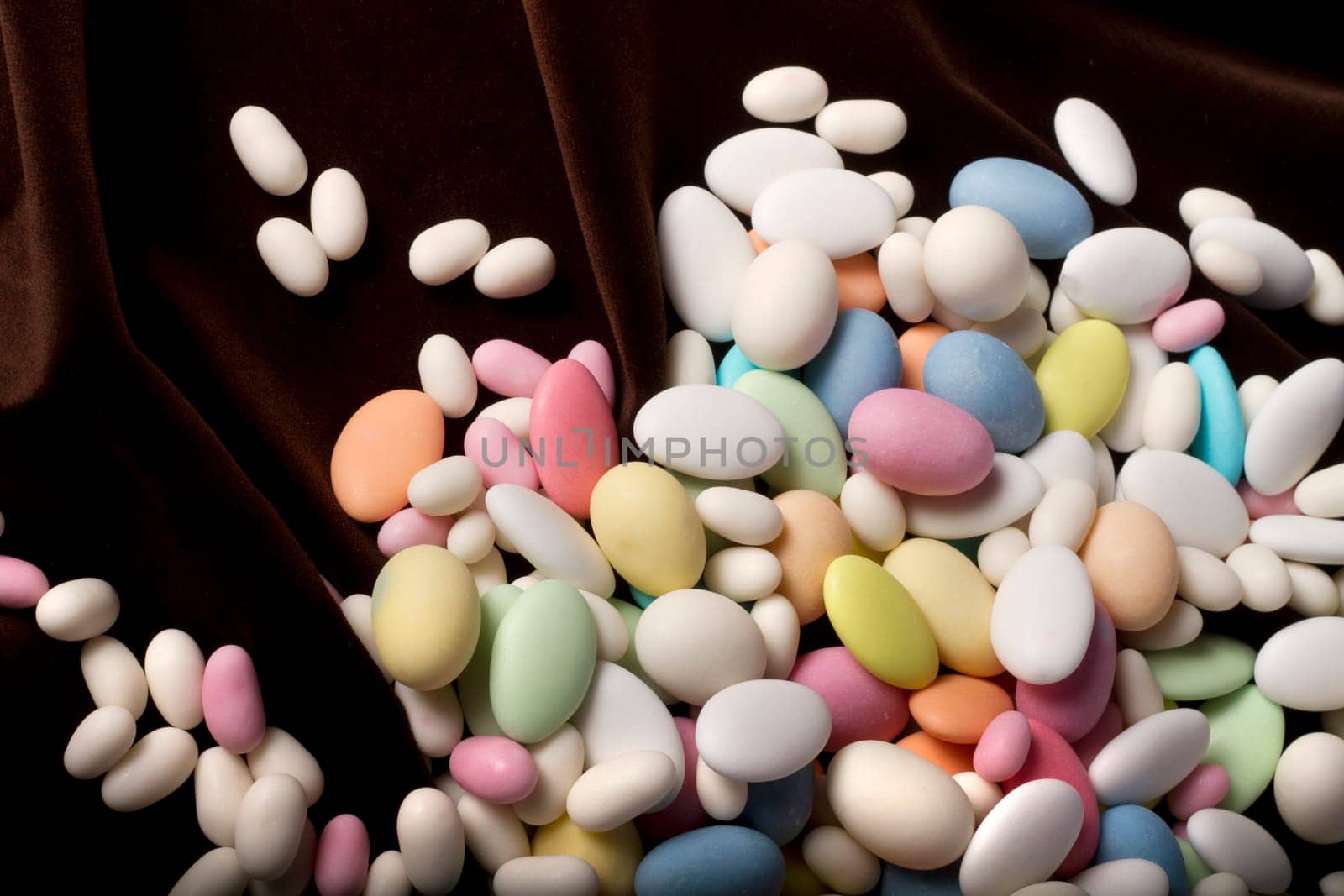 Close up view of a bunch of sweet almonds spread on a dark brown silk background.